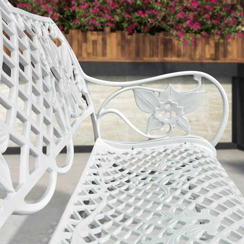 a close up of a white bench with flowers in the background