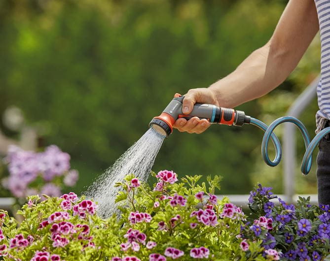 a person watering flowers with a garden hose