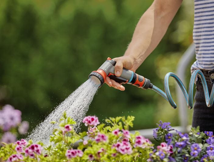 a person watering flowers with a garden hose